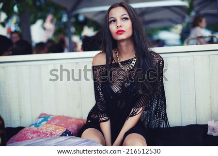 Brunette fashion girl seated in the terrace of beach cafe, beautiful brunette woman with red lips, model fashion woman outdoors seated in cafe