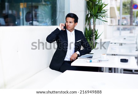 Attractive and handsome businessman using mobile phone, asian businessman having a phone talk, wealthy man talking on the smart phone seated in the terrace of  modern lounge cafe at his work break