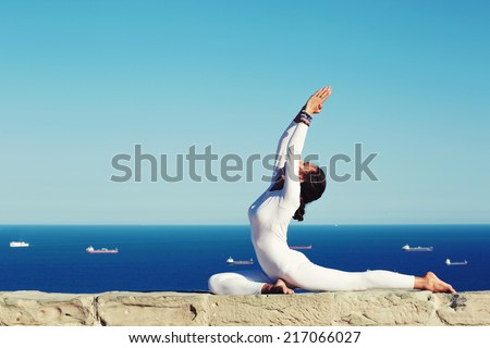 Beautiful woman in white clothes seated in yoga pose on blue sea background, slim woman with perfect body in meditation pose engage yoga, healthy woman in white clothes meditating and exercising yoga