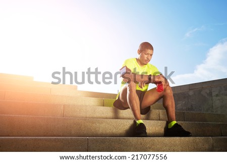 Handsome male runner very tired after run resting seated on the steps outdoors, male jogger with strong muscular body rest holding bottle of energy drink in the hands