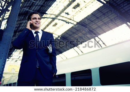 Traveling businessman talking on the mobile phone at metro station, handsome successful man in suit using mobile phone, male worker holding newspaper having a phone call