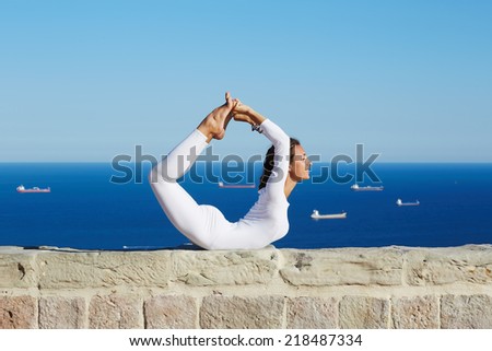 Healthy young woman makes yoga on high altitude with beautiful sea with ships on background, attractive woman practicing yoga enjoying sunny day at summer, yoga with amazing view of sea from high