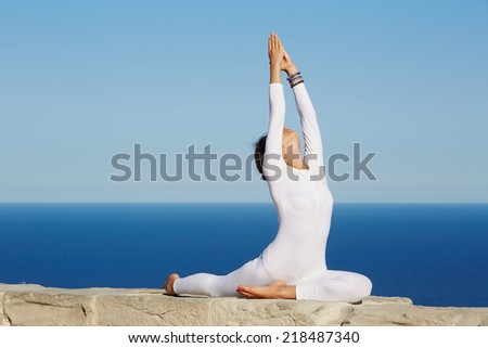 Pretty brunette woman makes yoga meditation at sunny evening outdoors, young slim girl makes yoga enjoying sunny day at summer with beautiful view of sea on background, feeling healthy with yoga