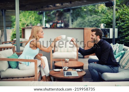 Confident business man and business woman at meeting outdoors, business partners smiling while drinking coffee and talking about good idea, young people clinking cups while smiling at business lunch