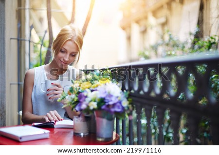 Attractive young girl reading book while drinking coffee at sunny day sitting on the balcony, beautiful young woman with cup of coffee on home balcony reading the book, female student reading book