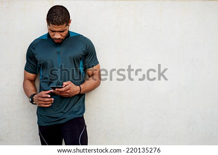 Handsome sportsman holding mobile phone and looking for the mobile screen standing outdoors, muscular build dark skin runner resting after run use his mobile phone, male runner using mobile phone