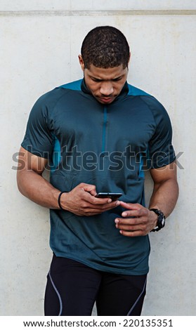Handsome sportsman holding mobile phone and looking for the mobile screen standing outdoors, muscular build dark skin runner taking break use his mobile phone, using technology concept