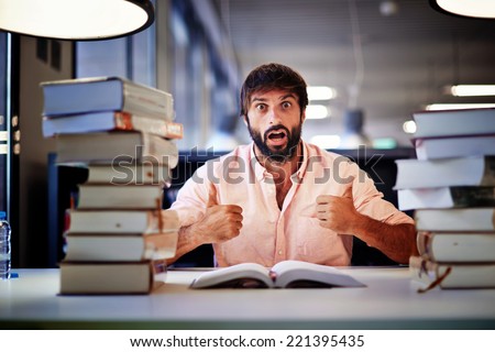 Attractive high school student ready for his final exam, surprise emotion face of student sitting at the library desk with two pile of books,student with two thumbs up make positive facial expressions