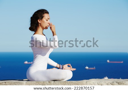 Woman seated in yoga pose on amazing sea background, yoga on high altitude with sea with ships on background, woman meditating yoga enjoying sunny evening, woman makes yoga meditation on high altitude