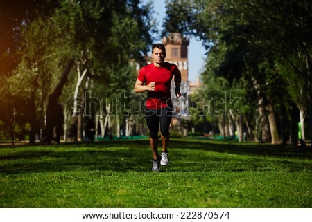 Athletic runner training in beautiful green park at sunny evening, fitness man running on green grass in the park, athletic sportsman with strong muscular body jogging outdoors, sports fitness concept