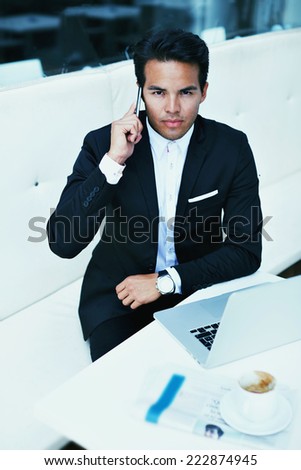 Asian businessman uses the new media technologies, young handsome man in a suit sitting in cafe talking on the phone, rich man calling on mobile phone, filtered image