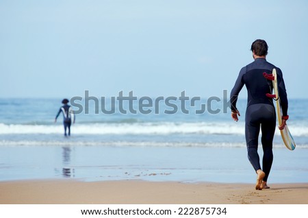 Handsome young surfer man walking at ocean beach holding his surfing board, muscular build surfer carrying surfboard while walking on the beach, men ready to surfing walk on the sand holding board