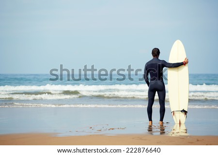 Athletic build young surfer holding surfboard while standing on the beach looking at ocean to find the perfect spot to go surfing waves, professional surfer waiting waves on the ocean beach