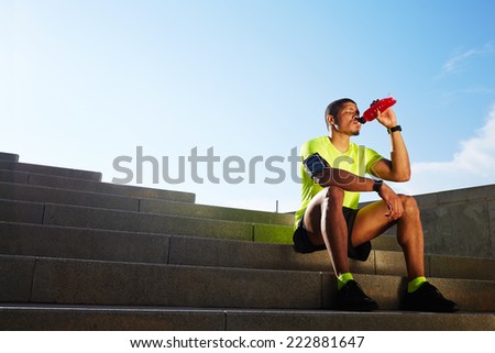 Handsome male runner seated on the steps drink water, beautiful fit man in bright fluorescent sportswear, sports fitness concept