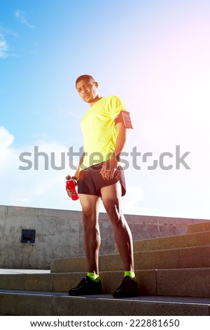 Dark skinned athletic runner with muscular strong body resting after jogging, beautiful fit man in bright fluorescent sportswear, sports fitness concept