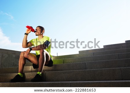 Handsome athletic runner seated on the steps drink water, beautiful fit man in bright fluorescent sportswear, sports fitness concept