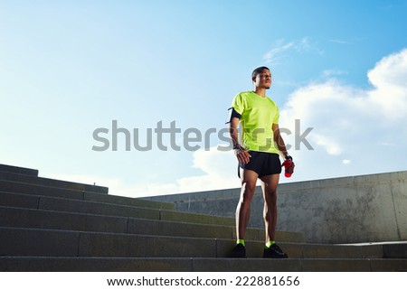 Male jogger taking break standing at orange summer sunset on the steps, beautiful fit man in bright fluorescent sportswear, sports fitness concept