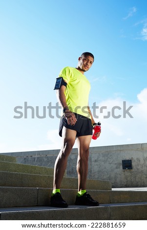 Sportsman holding bottle of water in the hand resting after run, beautiful fit man in bright fluorescent sportswear, sports fitness concept