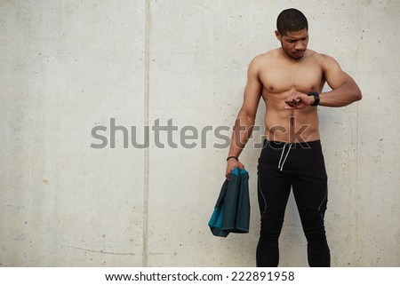 Male athlete looking to stopwatch and standing on background concrete wall, ready to start to run