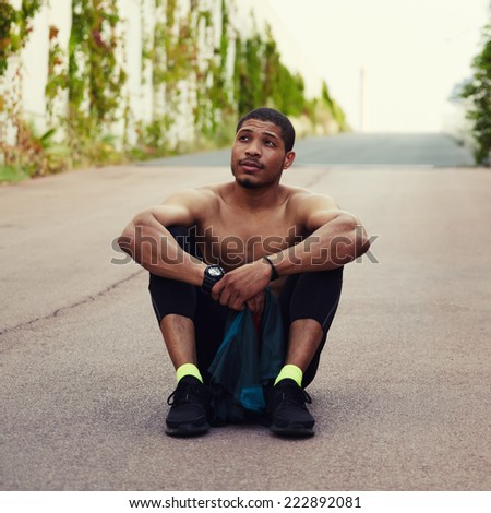 African athlete resting after evening run , sitting on the floor, on the road