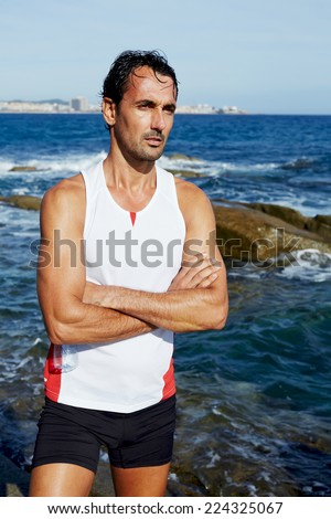 Portrait of athlete standing on sea rocks at sunny summer day while resting after intensive training outdoors, exhausted fit runner after workout resting on seaside, healthy lifestyle concept