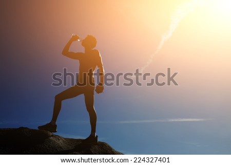 Silhouette of sporty fit man drinking water outdoor on sunny day, athlete refreshing with bottle of water after running