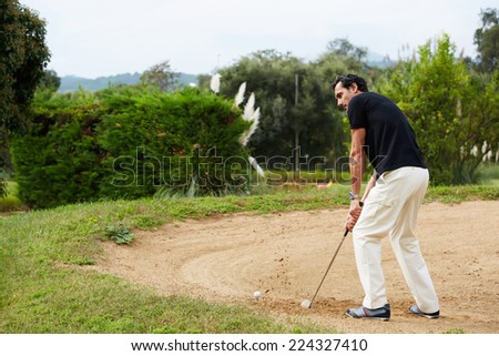 Adult man in sports clothing playing golf while standing golf sand trap, handsome adult man playing golf, attractive golfer hitting ball in action,rich wealthy man at leisure playing golf