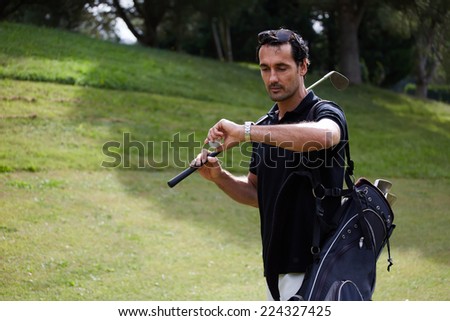 Attractive golf player checking the time while walk on beautiful golf course, male golf player at the course with a club sack, professional golfer carrying his bag while walking to the next hole