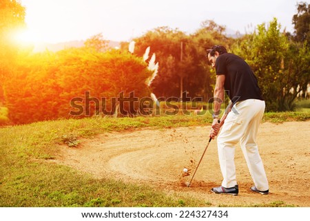 Man hitting golf ball from sand trap at sunny evening, rich adult man playing golf, strong golf shot in action,wealthy man at recreation playing golf on green course,golfer hitting ball in action