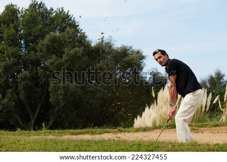 Professional golf player in action hitting golf ball, strong golf shot of handsome adult player standing on beautiful golf course