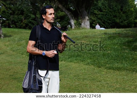 Handsome wealthy man in polo t-shirt standing on golf course holding ball an golf driver, success attractive man playing golf at leisure on holidays, success and welfare concept