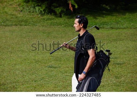 Confident male golfer holding driver and black golf bag while walking on green course at sunny day, male golf player at the course with a club sack, golfer carrying his bag while walking to next hole