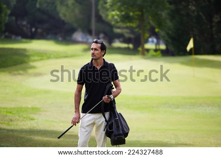 Success attractive man playing golf at leisure on holidays, success and welfare concept, handsome wealthy man in polo t-shirt standing on golf course, male golf player at the course with a club sack