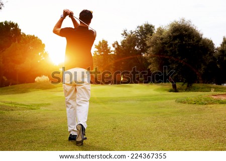 Good strike, golfer swinging his driver and looking away while standing on golf course, professional golfer looking trajectory of the ball, golfer hitting golf ball standing on course at sunny evening