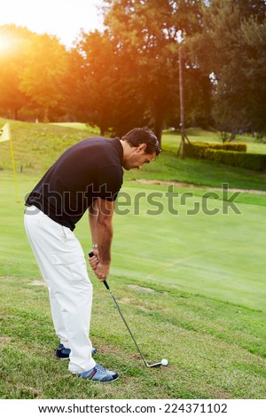 Attractive golfer hitting with club standing on the course, golf player take a shot, holidays leisure of wealthy man