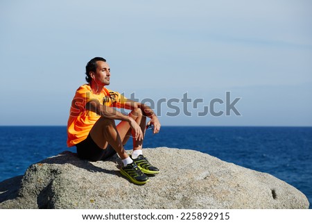 Sportsman listening to music on headphones outdoors, rest and relax after the training, male jogger seated on the beach enjoying music, fit man listening to music on mobile smart phone,sport lifestyle