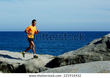 Young athlete running fast jumping over rocks with beautiful sea horizon on background