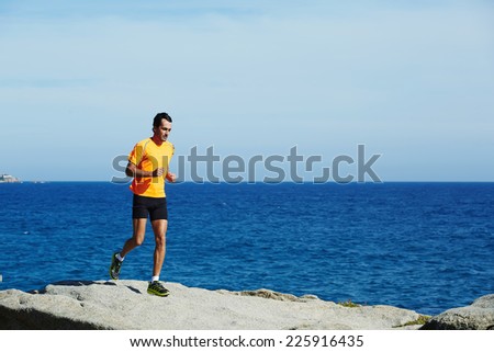 Male jogger in fluorescent t-shirt runs over sea rocks at morning training outdoors