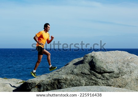 Male jogger in bright fluorescent sportswear running over rocks along the beach