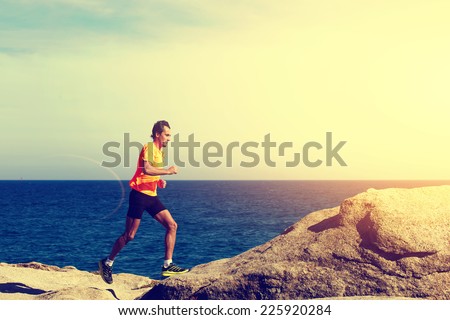 Athlete man in bright fluorescent t-short running fast along the sea at sunset
