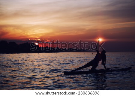 Yoga training in harmony with nature, silhouette of yoga woman holding light in the hand, spiritual concept, paddle board yoga performed by beautiful woman with bright sunset on background