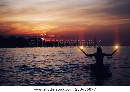 Silhouette of woman holding lights in the hands during sup yoga meditation, yoga training in harmony with nature, silhouette of paddle board yoga performed by beautiful woman, spiritual concept