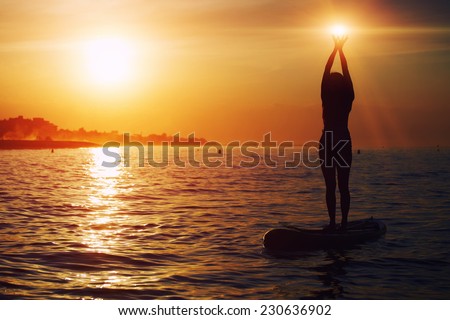 Yoga training in harmony with nature, silhouette of yoga woman holding lights in the hands, spiritual concept, stand up paddle board yoga performed by beautiful woman with bright sunset on background