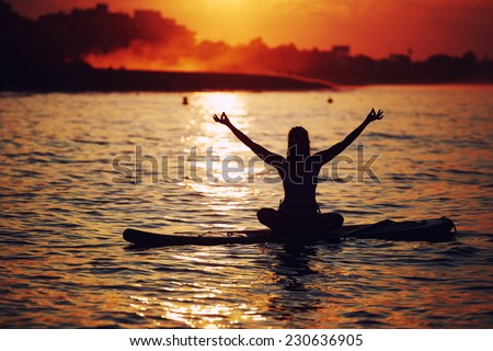 Harmony with the nature in yoga meditation, silhouette of woman doing paddle board yoga with beautiful orange sunset light reflected on the water, paddle surf yoga at the amazing sunset over the sea