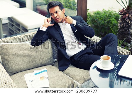 Attractive and handsome businessman using mobile phone, asian businessman having a phone talk, wealthy man talking on the smart phone seated in the terrace of modern lounge cafe at his work break