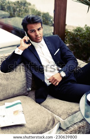 Attractive and handsome businessman using mobile phone, asian businessman having a phone talk, wealthy man talking on the smart phone seated on sofa in modern lounge cafe at his work break