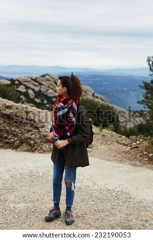 Young hipster girl standing on mountain road looking away, on high altitude female hiker walking, adventure walk in mountains with hipster girl