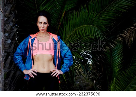 Portrait of confident sporty woman standing with hands on the belt resting after run, beautiful sport fashion model,attractive fit woman with sexy abdominal looking to the camera resting after workout