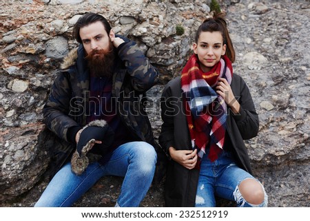 Beautiful man and woman taking a break sitting on rock cliff during mountains hike, attractive man with beard resting tires after hike, beautiful hipster girl dressed in grunge style clothes hiking