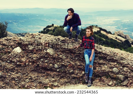 Couple of hikers resting sitting on mountain hill with beautiful view on background, stylish teenager guys sitting on the rock, cute and stylish romantic couple at holidays leisure like county style